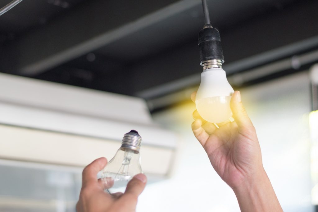 A person exchanges a fluorescent light bulb with a new LED light bulb, an example of LED retrofitting.