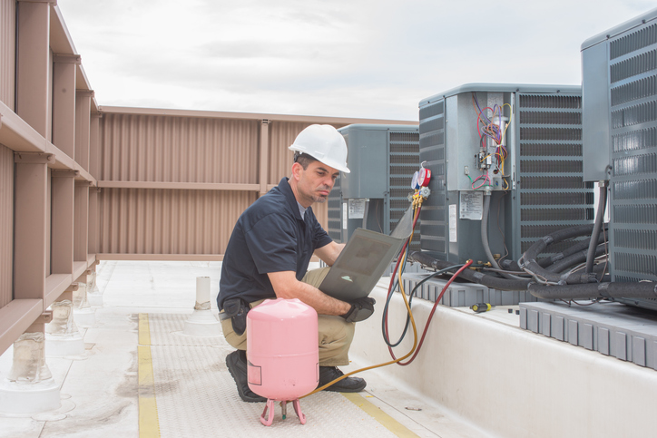 Technician looking at a panel off a condensing unit is one componenent of commercial hvac preventive maintenance cost